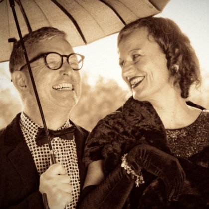 Die Chansonetten im eleganten Abendkleid und mit Fliege unter ihrem Pagodenschirm lachen sich an.
